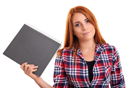 Cheerful young redhead woman in plaid shirt holding a notebook, copybook, folder in the hand, isolated on white background. Education, study, exams, achievement concept.の写真素材