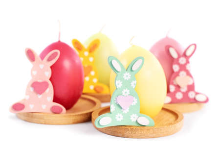 Close up of small Easter Bunnies next to egg shaped candles in pastel colors, isolated on white background. Fun and colorful Easter celebration concept.の写真素材