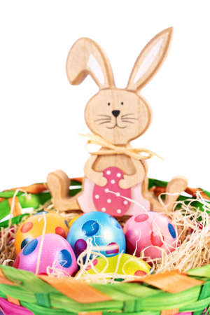 Close up of colourful Easter eggs with polka dots in a basket together with a toy Easter bunny, isolated on white background. Fun and colourful Easter celebration concept.の写真素材