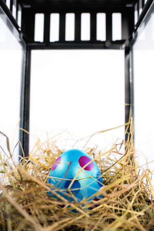 Close up of a beautiful colourful Easter egg in a nest within a decorative lantern, isolated on white background. Fun and colourful Easter celebration concept. Easter decoration concept.の写真素材