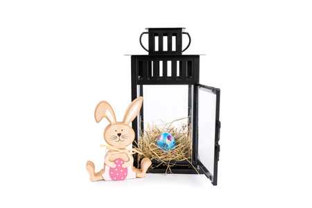 Wooden Easter bunny with a colourful Easter egg in a nest within a decorative lantern, isolated on white background. Fun and colourful Easter celebration concept. Easter decoration concept.の写真素材