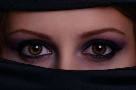 Close up portrait of a gorgeous female face with crystal and shiny eyes with beauty make up, wearing black scarf niqab hijab around her face. Burqa, hijab, niqab. Arabic, mysterious, authentic, mystic, beauty, fashion.の写真素材
