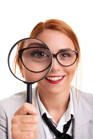 Close up of a beautiful young businesswoman smiling and looking through magnifying glass, isolated on white background. Analysis, scrutiny concept.の写真素材