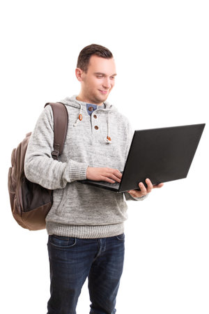 Portrait of a young male student with a backpack holding a laptop computer, isolated on white background. Young guy in casual clothing and backpack holding and using open laptop.の写真素材
