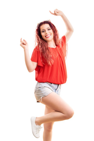 Beautiful redhead woman with long wavy hair in a fashionable summer outfit jumping out of happiness, isolated on white background. Summer, enjoying concept.の写真素材