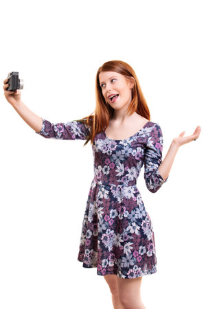 Beautiful young woman in a flowery dress taking a selfie or filming her self, isolated on white background. Attractive redhead girl with long hair vlogging. Lifestyle, happiness, and social concept.の写真素材
