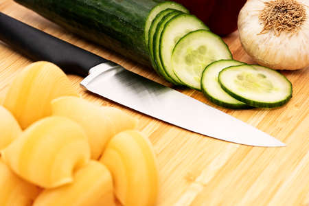 Chopped cucumber on wooden cutting board with knife and assorted fresh vegetables. Diet and vegetarian food preparing, meal cooking concept, healthy lifestyle.の写真素材