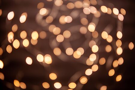 A background with a golden bokeh on a dark substrate. Garland lights, yellow glare, abstract pattern of lit lights in warm tones. Real optical bokehの写真素材