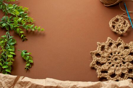 Knitted lace jute washcloth, craft paper, green plant on a brown background. Concept zero waste, hand made, knitting, DIY の写真素材