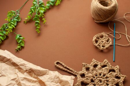 Knitted lace jute washcloth, craft paper, green plant on a brown background. Concept zero waste, hand made, knitting, DIY の写真素材
