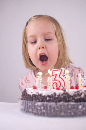 Happy caucasian toddler girl celebrates birthday, cake, blowing out candlesの写真素材