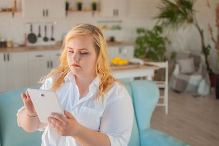 Young beautiful overweight woman makes online order in living room at homeの写真素材