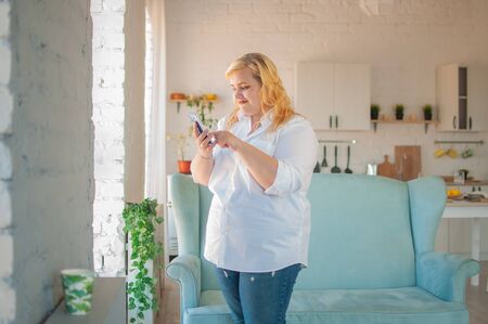 Young beautiful overweight woman makes online order in living room at homeの写真素材