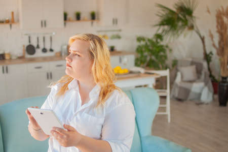 Young beautiful overweight woman makes online order in living room at homeの写真素材