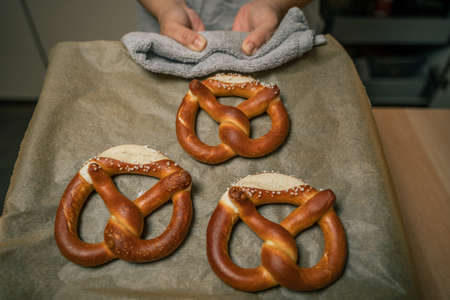 Woman holds baking tray with three freshly baked pretzels in handの写真素材