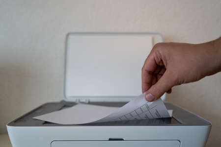 Hand puts a sheet of paper in the printer to copy itの写真素材