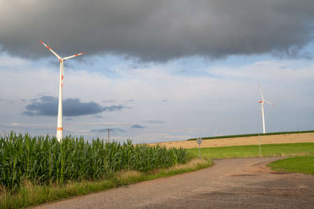 Dark clouds over landscape with two wind turbines, cornfield, agriculture fields and a country road