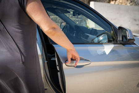 Young woman in gray dress opens passenger door of a silver car