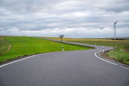 Curvy road in the landscape with a cloudy sky on a cold windy autumn dayの写真素材