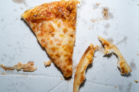 A piece of leftover margherita pizza and 2 crusts on a white pizza box