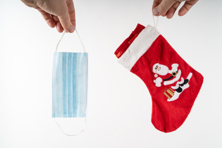 Hands holding a blue medical protective mask and a red Christmas stocking with a Santa Clausの写真素材