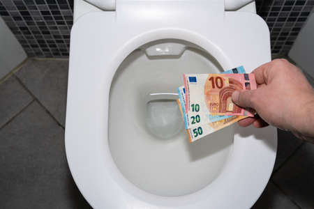Male hand holds euro banknotes in a toilet bowlの写真素材