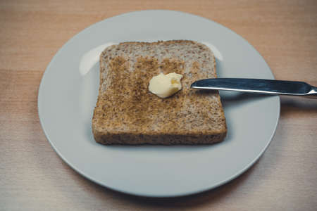 Toasted whole wheat toast bread with a stick of butter on the plate and a knife by the side for breakfastの写真素材