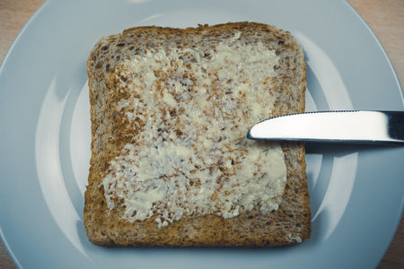 Whole grain toast bread smeared with butter on a white plate and a knife on the sideの写真素材