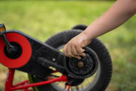 Boy holds the training wheel from his bike with a dirty handの写真素材