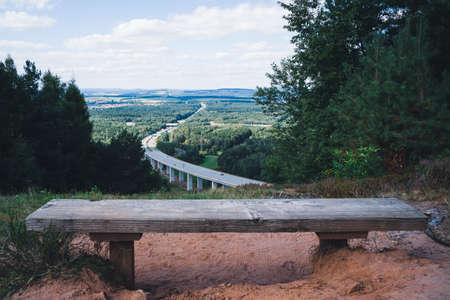 Wooden bench overlooking a highway bridge between tress in the forestの写真素材
