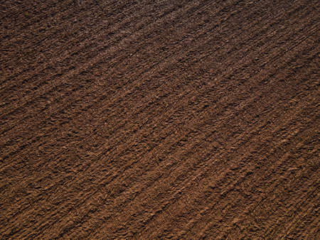 Drone shot of freshly plowed field with brown soil in spring