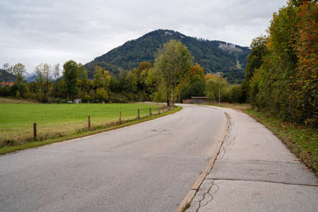 Rural road with meadow on the left, trees on the right and mountains in the background on a cold autumn dayの写真素材