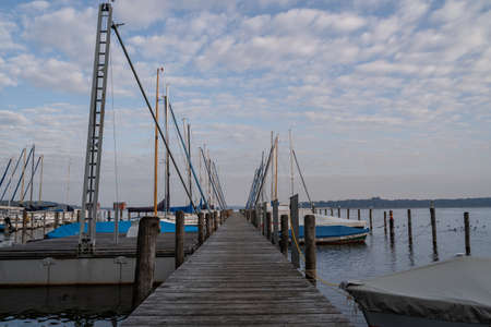 Roped up and covered sailboats on the wooden jetty in the lake in the morningの写真素材