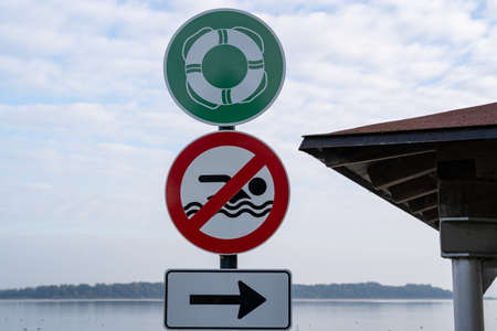 Green sign with a swimming ring, red sign with a crossed out swimmer and white sign with an arrow pointing to the right on a post at the lake beachの写真素材