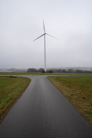 Walkway in the landscape with a wind turbine in the distance on a foggy day in December