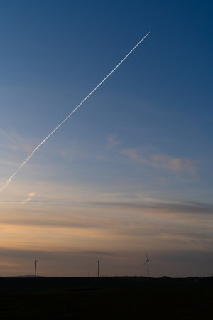 Sunset in the countryside with wind turbines and a plane with contrails in the blue skyの写真素材
