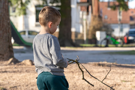 5 year old boy plays with 2 wooden twigs in the playgroundの写真素材