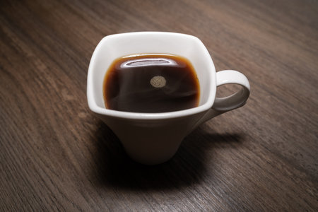 White square cup with hot black coffee on wooden tableの写真素材