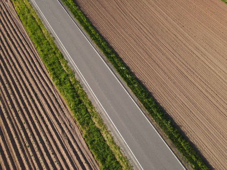 View from above of an asphalt road between plowed agriculture land with soil in the landscapeの写真素材