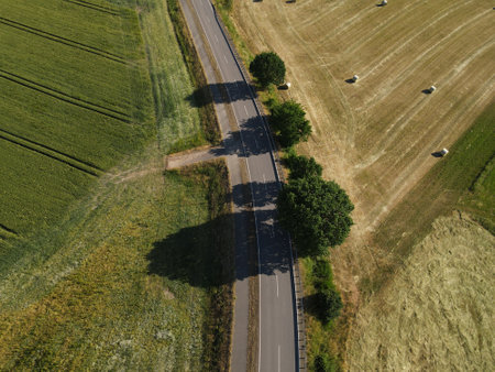 Aerial view of a rural road between crop fields and mowed fields with hay bales in the landscapeの写真素材