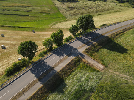 Aerial view of an asphalt road between grass and haybales in the countryside on a sunny day in springの写真素材