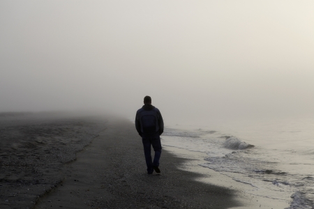 Lonely man walking on a foggy beachの写真素材