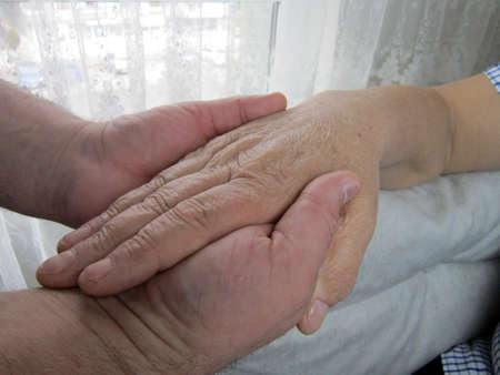 Hands of young man holding an old person's hand for kissing. Parents, regards.の写真素材