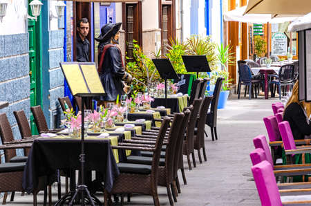 A waiter is standing in the outer doorway of a restaurant, looking at the very nicely decorated but empty tables.のeditorial素材