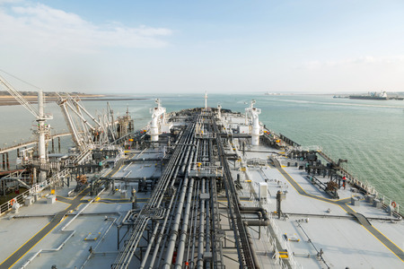 Oil product tanker during cargo operation moored to the jetty with connected cargo line to the terminal.の写真素材