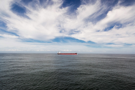 Seascape with a red cargo ship under cloudy sky.の写真素材