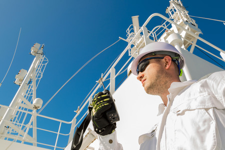 Deck officer speaking by VHF on radar deck under blue sky