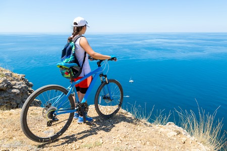Girl with a bike at the edge of the shore is looking to the ocean.の写真素材