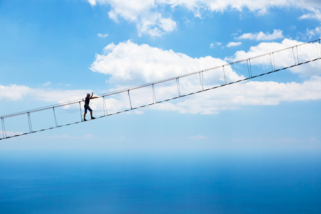 Man climbing on the suspension bridge to the peak of mountain.の写真素材