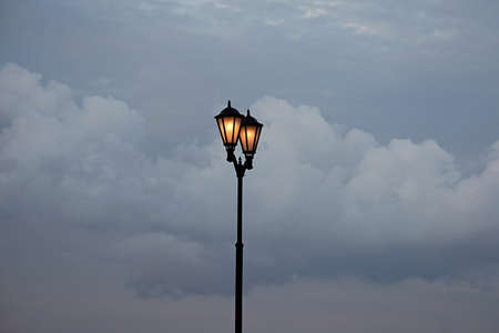 street lamp with lamps on against a background of dark clouds at dusk.